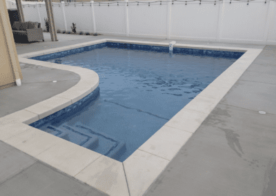 A swimming pool in a backyard with a white fence.