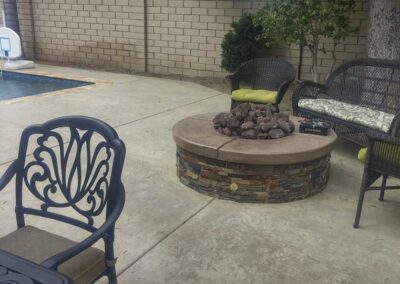 A patio with a fire pit and chairs near a pool.